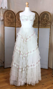 An original vintage 1950's strapless wedding dress in ivory and pink lace is shown inside a wedding dress shop