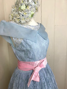 A pale blue vintage dress with a wide collar and a pink sash makes a charming picture on a vintage dummy. The details of the lace pattern can be clearly seen.
