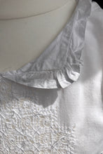 The collar of a white linen vintage tunic is shown, with incredible drawn threadwork detailing.