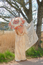 A beautiful boho bride stands on a country lane. She wears a floor sweping, backless vintage lace gown and carries a pretty antique parasol