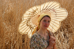 Little house on the prairie style - a pretty girl with a yellow headscarf around her head is framed by a parasol. She wears an original vintage 1940's dress with a paisley print