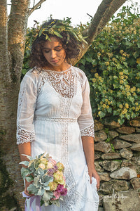 A beautiful model stands in a shaft of autumnal evening light , wearing a white cotton lawn Edwardian antique dress with Bedfordshire lace, broderie cut work, tape work and hand embroidered details