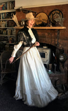 A prairie cowgirl bride smiles mischeviously as she swings her skirts. She is wering a bridal cowgirl hat and carrying a horde whip 