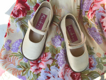 Cream silk bridesmaids shoes for a child are shown against a floral fabric