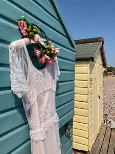 A white lace dress over a soft pink slip is hung on the door of a teal beachhut