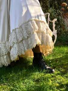 The details of the antique lace frills on the silk skirt are shown, delicate lace dripping in heavy folds. A laced boot and sturdy woollen stockings are just visible