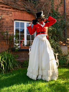 A striking model wears a red Victorian military jacket over an ivory Victorian wedding dress. The look is finished with a battered black top hat and antique lace veil. The look could be described as steam punk bride. 