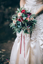 The ruched oyster satin of a vintage wedding gown is contrasted with a bouquet of cream and red roses and silvery greenery